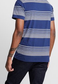 Kortärmad blå t-shirt med horisontella vita ränder, rundad halsringning och rak fåll. Bomullstyg med en slät yta.