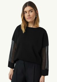 Schwarzer Pullover mit transparenten schwarzen Mesh-Ärmeln, rundem Ausschnitt und lockerer Passform. Weicher Textur mit kontrastierenden Materialien.