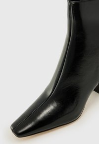 Stivale alla caviglia in pelle nera con punta affusolata, texture liscia e design elegante. Presenta una leggera lucentezza e un tacco blocco di altezza media.