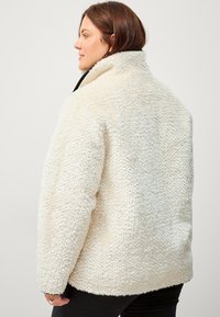 Crème-kleurige fleece jas met een gestructureerde, fluffy buitenkant, hoge kraag en zijzakken. Ontspannen pasvorm, verlaagde schouders en gestikte naden.