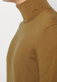 Bruine turtleneck trui van ribstof, met een subtiele "HUGO"-logo op de halslijn en een strakke pasvorm met lange mouwen.