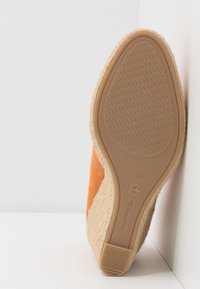 Semelle d'espadrille orange taille 37 avec semelle en caoutchouc, semelle intermédiaire recouverte de jute et marquage Tamaris appuyée contre un mur blanc.
