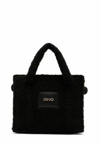Sac noir en tissu texturé avec une apparence duveteuse, doté de deux poignées robustes et d'un patch en cuir noir avec un logo doré.