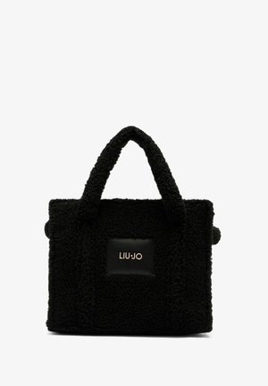 Schwarze Tasche aus strukturiertem Stoff mit flauschigem Aussehen, ausgestattet mit zwei robusten Griffen und einem schwarzen Lederpatch mit goldfarbenem Logo.