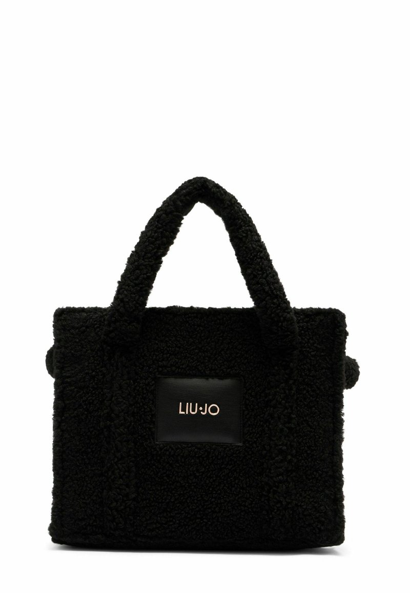 Sac noir en tissu texturé avec une apparence duveteuse, doté de deux poignées robustes et d'un patch en cuir noir avec un logo doré.