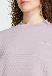 Lila strukturerad träningsskjorta med rund halsringning och präglat mönster, med en liten vit "TERREX"-logga på vänster bröst.