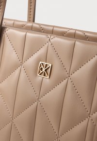 Bežasta usnjena torbica s kvadratnim vzorcem, opremljena s pozlačenimi dodatki in geometrijskim logotipom. Gladka tekstura in trpežni ročaji.