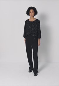 Musta teksturoitu yläosa hopeisilla pilkkuilla, yhdistettynä mustiin räätälöityihin housuihin. Asussa on rento istuvuus ja housuissa on hienovaraisia yksityiskohtia.