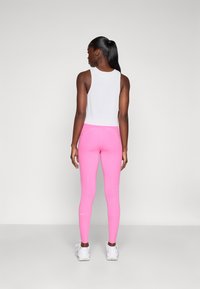 Rosa treningsleggings med perforerte detaljer nederst på bena, kombinert med en hvit ribbet tanktopp. Hvite joggesko fullfører antrekket.