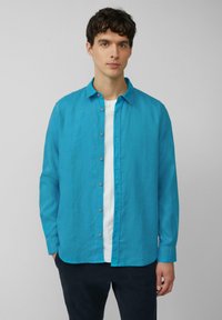 Turquoise overhemd met een spread collar, gemaakt van lichtgewicht stof, met lange mouwen en knoopdetails, gedragen over een wit T-shirt.