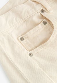 Krämfärgade jeans med en texturerad yta, med en liten ficka och metallknappar på midjebandet.