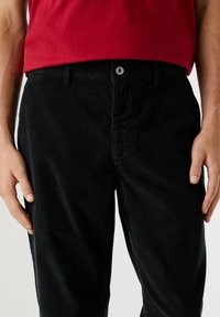 Zwarte corduroy broek met een rechte pasvorm, voorzien van een knoopsluiting aan de voorkant, riemlussen en een subtiele ribbeltextuur.