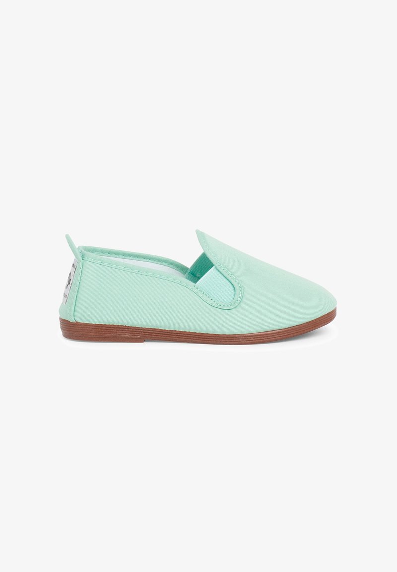 Chaussure slip-on vert clair avec panneau latéral élastique et semelle plate marron, vue de profil sur fond blanc.