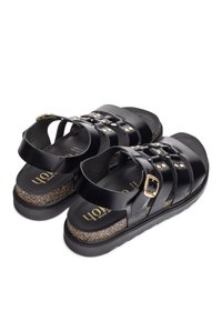 Sandalias negras con múltiples tiras, hebillas doradas, plantilla de corcho, suela plana y acabado texturizado. Diseñadas para comodidad y apoyo.