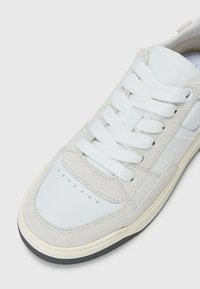 Lichtgrijze sneaker met een mix van suède en leer, ronde neus, witte veters en een contrasterende beige zool met een gestructureerde grip.