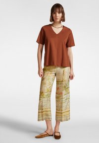 Una maglietta marrone a manica corta con scollatura a V abbinata a pantaloni larghi a fantasia con colori tenui e disegni floreali, completata da ballerine marroni.