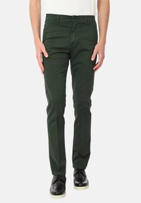 Chino in cotone verde scuro con vestibilità slim, chiusura a bottoni e zip, passanti per cintura e tasche laterali, abbinati a scarpe nere.