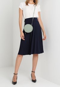 Laivastonsininen laskostettu hame korkealla vyötäröllä, yhdistettynä istuvaan valkoiseen lyhythihaiseen paitaan ja vaaleanvihreään pyöreään olkalaukkuun. Mustat korkokengät.