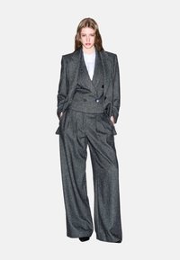 Blazer tailored a righe grigie e pantaloni a gamba larga, con un gilet doppiopetto, il tutto in un tessuto testurizzato con una silhouette strutturata.