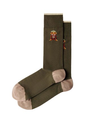 Chaussettes vert olive avec des orteils et talons beiges, ornées d'un petit chien brodé portant un pull et un chapeau rouges près du haut.