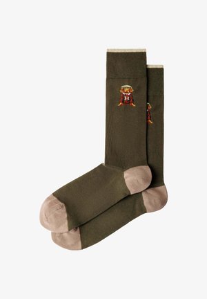 Calcetines verde oliva con dedos y talones beige, con un pequeño perro bordado que lleva un suéter y un sombrero rojo cerca de la parte superior.