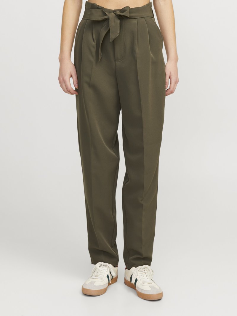 Pantalon taille haute vert olive avec plis et ceinture nouée, porté avec des baskets blanches par une personne debout sur un fond uni.