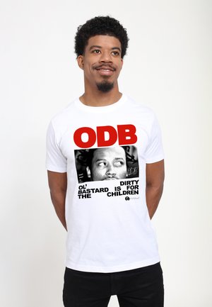 Mann mit kurzen lockigen Haaren, der ein weißes T-Shirt mit rotem "ODB"-Text und einem schwarz-weißen Foto eines Männergesichts trägt.