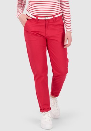 Person trägt rote Hose mit hochgekrempelten Bündchen, einen weißen geflochtenen Gürtel, weiße Turnschuhe und ein rot-weiß gestreiftes Langarmshirt.