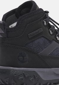 Černá obuv Timberland s texturovaným materiálem, gumovou podrážkou a logem. Obsahuje systém šněrování a vzorované polstrování pro pohodlí. Voděodolný design.