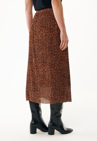 Jupe plissée marron avec un motif léopard, associée à des bottes noires à talons hauteur genou. Le tissu a une texture lisse et des couleurs vives.