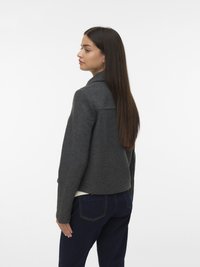 Grijze wollen jas met een ingesneden kraag, licht ingekort model en lange mouwen, gecombineerd met donkerblauwe spijkerbroek. Gladde textuur.