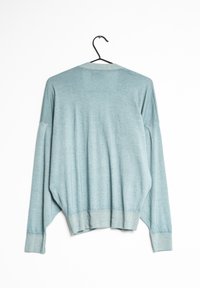 Suéter azul claro de gran tamaño con dobladillo acanalado, cuello redondo y mangas largas. Está hecho de una tela suave y texturizada. cuelga de un gancho negro.