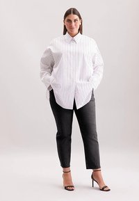 White button-up shirt with vertical navy stripes, paired with dark gray tapered pants and black strappy heels. Fabric appears smooth and crisp.