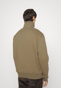 Sweatshirt pullover vert olive avec col montant, poignets côtelés et coupe décontractée, fabriqué en tissu doux. Texture lisse, détails minimalistes.