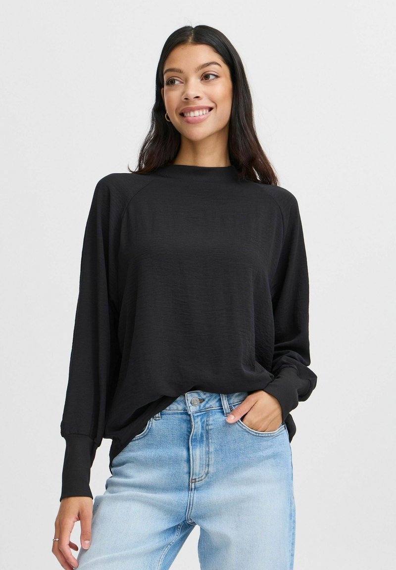 Top nero a maniche lunghe con collo alto e polsini a costine, caratterizzato da una vestibilità comoda e una texture leggera, abbinato a jeans in denim azzurro chiaro.
