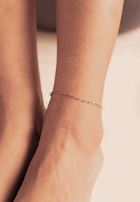 Una pulsera de tobillo de cadena de oro descansa sobre un tobillo de tono de piel clara, presentando eslabones delicados y un simple cierre. Se puede ver la textura suave de la piel.