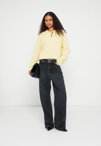 Light yellow long-sleeve polo shirt with three buttons, paired with high-waisted dark gray wide-leg jeans. Black handbag accessory.