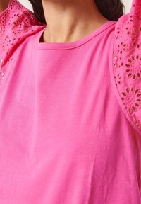 Camiseta de algodón rosa con mangas de encaje con ojales y recortes florales. Textura suave, escote redondo y diseño de corte relajado.