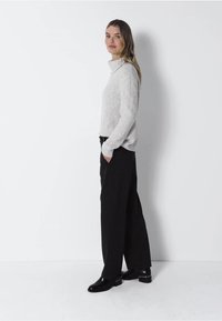 Ljust grått stickat tröja med hög krage, matchat med svarta vida byxor och svarta ankelstövlar. Enkel, texturerad design.