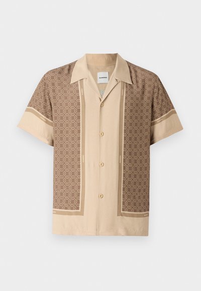 Chemise à manches courtes beige avec des motifs géométriques marron, dotée d'un col en V, d'une fermeture à boutons et d'une texture de tissu lisse.