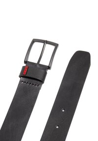 Cinturón de cuero negro con una hebilla de metal negro mate, diseño de correa plana y detalle de costura cerca de la hebilla. Incluye agujeros de ajuste.