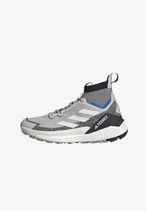 Scarpa atletica grigia con design alto alla caviglia, tomaia in mesh, strisce bianche, suola strutturata e dettaglio nero sul tallone con la scritta "TERREX".