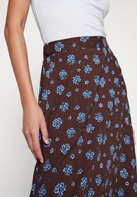Falda marrón con estampado floral que presenta pequeñas flores azules, tejido de tela entrelazada, se abre suavemente, con una textura suave y una cintura ajustada.