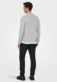 Pull en maille gris avec un col côtelé, porté sur une chemise blanche, associé à un pantalon noir et des chaussures sombres, vu de dos.
