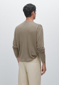 Långärmad, brun stickad skjorta gjord av mjukt tyg; har en avslappnad passform med lätt samlade ärmar och rund hållare.