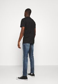 Camiseta de algodón negra, de mangas cortas, combinada con unos vaqueros de mezclilla azul claro y zapatillas altas negras. Enfócate en un diseño limpio y sencillo.