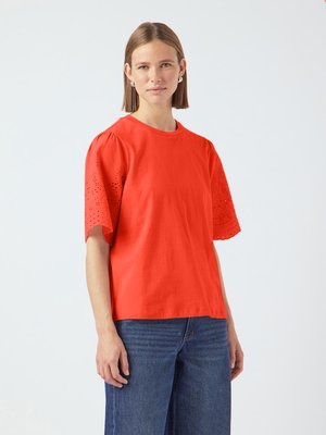 T-shirt en coton rouge avec des manches courtes bouffantes et des détails en découpes œillets, associé à un jean en denim bleu. Design simple et décontracté.