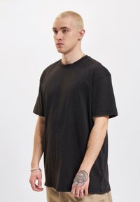 Tricou din bumbac negru, supradimensionat, cu guler rotund, mâneci scurte și un finisaj texturat, purtat de un model masculin pe un fundal simplu.
