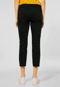 Czarne krótkie spodnie o gładkiej fakturze, z szlufkami na pasek i dwoma tylnymi kieszeniami. W zestawieniu z jasnymi butami.