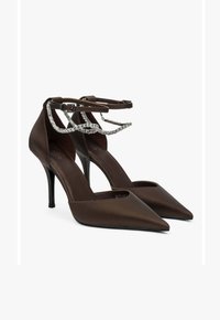 Brown satin high-heeled pumps with pointed toes, ankle straps, and sparkling silver chain accents. Smooth texture and sleek design.